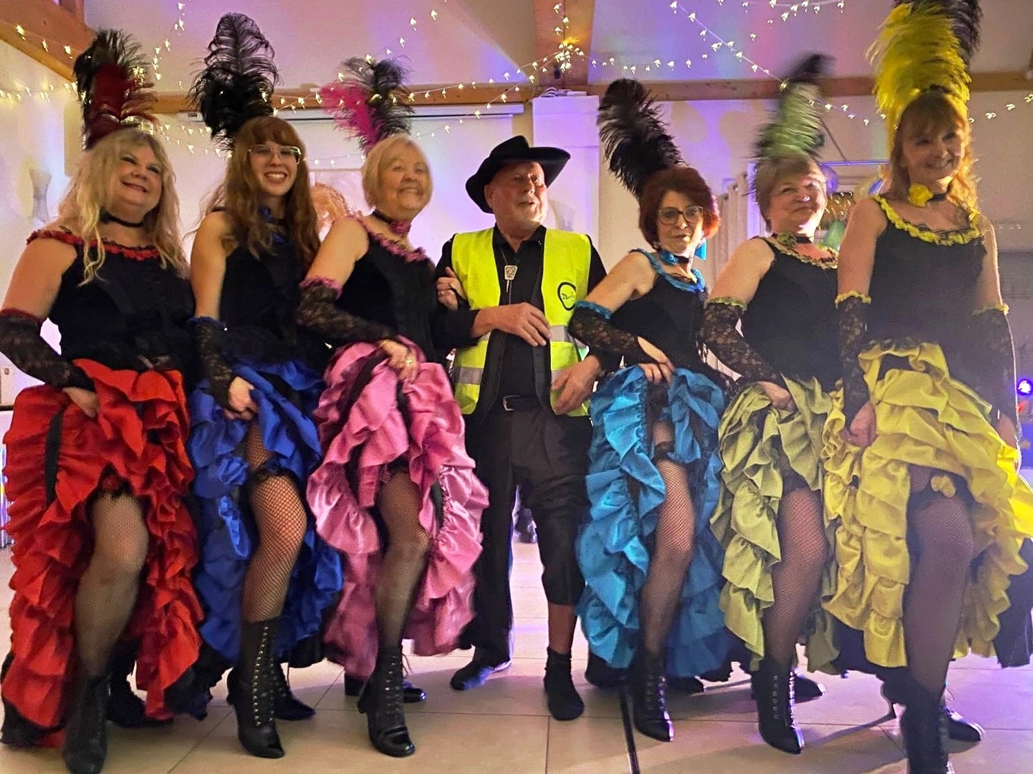 Texas Outlaws - Line dance club - Eine Gruppe von Personen in Tanzkostümen posiert gemeinsam; zu sehen sind Frauen in gerüschten Cancan-Röcken sowie ein Mann in Warnweste und Cowboyhut.